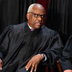 Clarence Thomas seated in black robes speaking with Chief Justice John Roberts