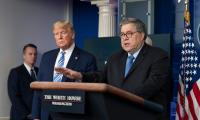 William Barr speaking at a podium while Donald Trump looks on from the background