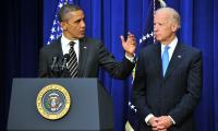 Barak Obama standing at a podium gesturing with Joe Biden standing to his right with his hands folded in front of him.