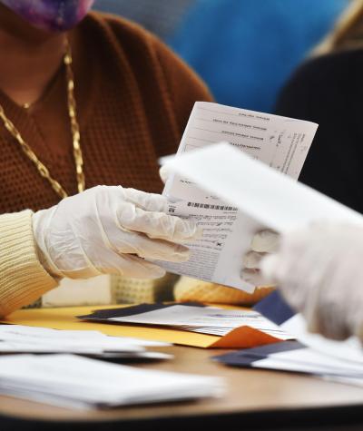 People wearing latex gloves open ballots