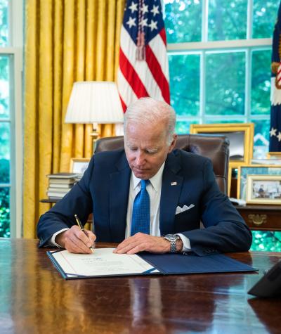 President Joe Biden sitting at his desk in the Oval Office signing a document