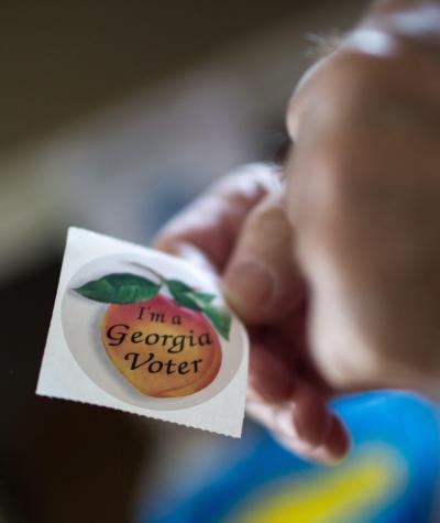 Hands holding a sticker with a peach on it that says "I'm a Georgia Voter"